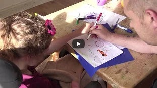 Criança desenhando e colorindo papel em uma mesa de madeira.